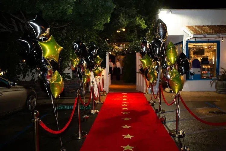 Red-carpet entrance at night with gold and black balloons, velvet ropes, and a lit building entrance