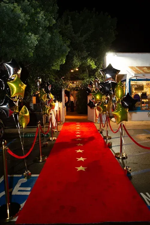 Red carpet with gold stars and balloon-lined entrance leading to a lit building at night