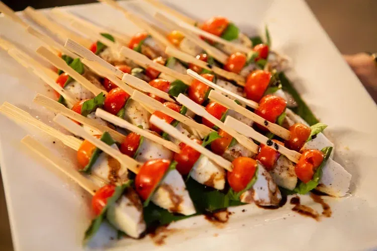 Grilled vegetable skewers drizzled with sauce on a white platter