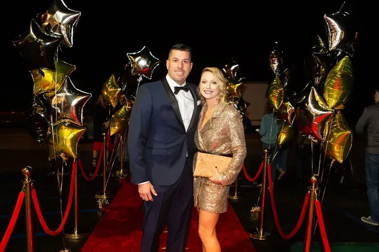 Couple posing on red carpet with gold and black balloon decorations and red ropes
