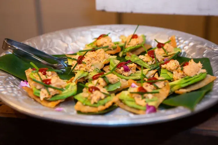 Plated appetizer of green wrapped bites topped with herbs and red garnish on a silver dish
