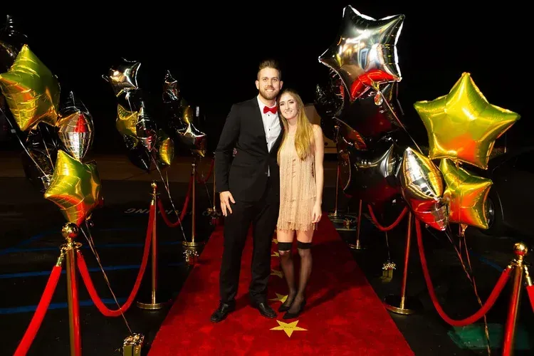 Couple on a red carpet with gold star balloons and velvet ropes at a formal event