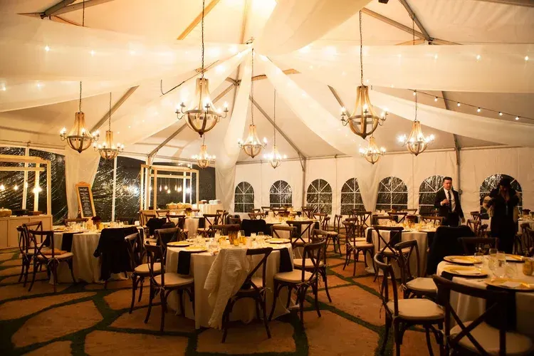 Elegant tented banquet hall with round tables, chandeliers, and warm lighting