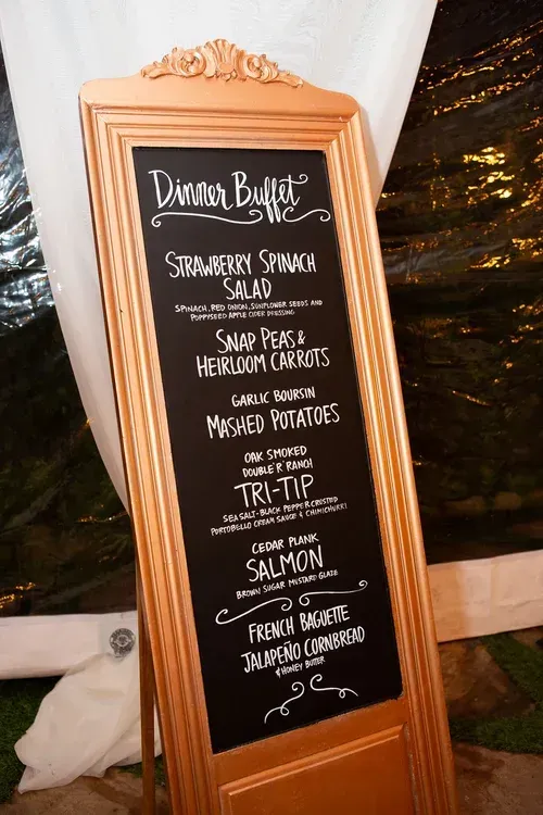 Wood-framed chalkboard menu sign at an event, listing dinner buffet items in white chalk