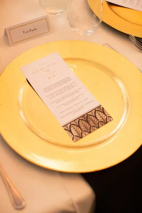 Yellow dinner plate with a menu card on a set table, beside a wine glass and silverware
