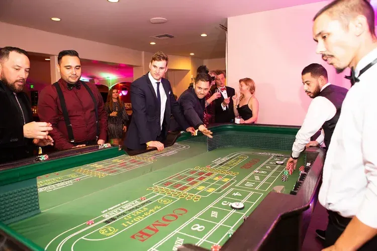 People gathered around a green casino table, watching a game in a warmly lit room.