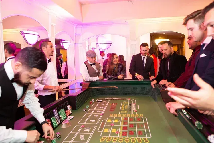 People gathered around a casino roulette table in a brightly lit room, watching the game.