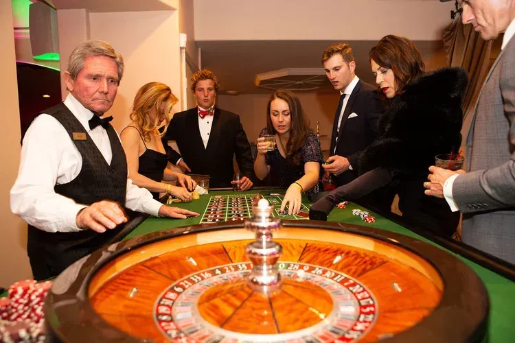 People gathered around a roulette table at a casino, with a croupier in a black vest