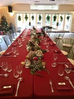 Long banquet table with red tablecloth, glassware, and holiday greenery in a bright decorated room