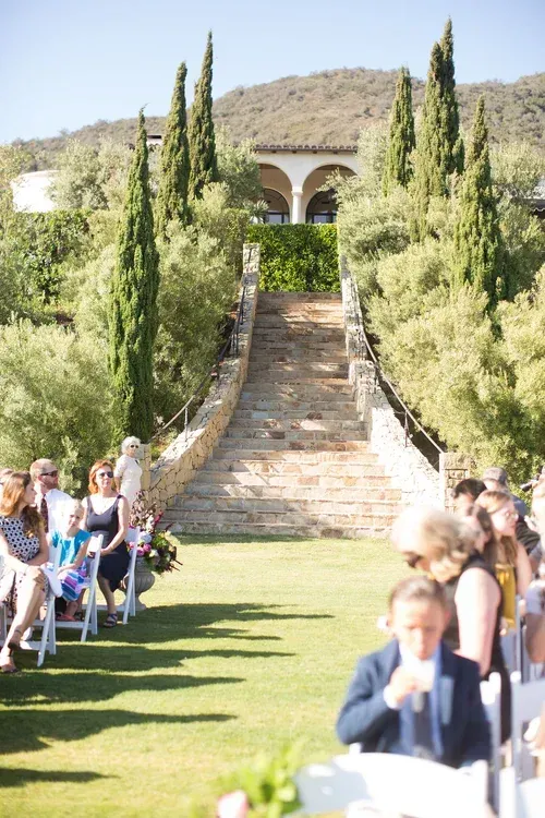 Outdoor wedding aisle with stone steps, green lawn, and guests seated on both sides.