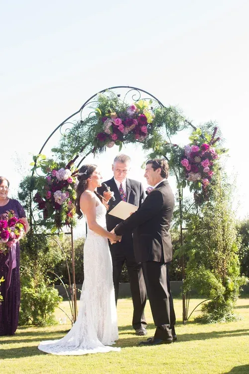 Outdoor wedding ceremony under a flower arch, couple exchanging vows before an officiant