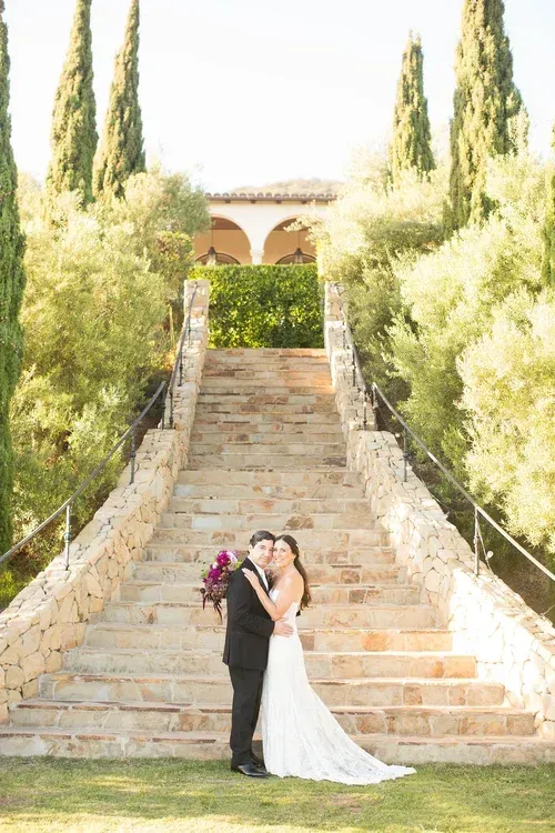 Bride and groom embracing on stone steps in a sunlit garden venue
