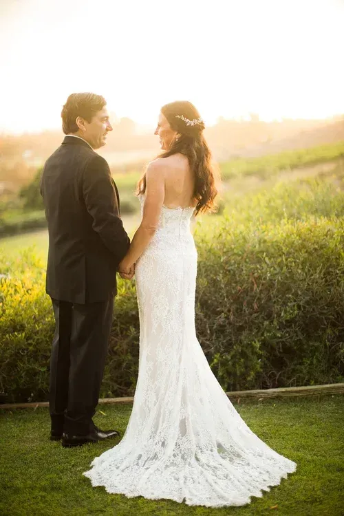 Bride and groom standing together outdoors at sunset, facing each other in a grassy field.