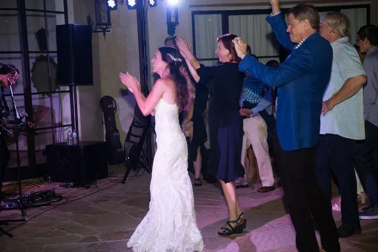Guests dance at a formal indoor reception, with a bride in a white dress in the foreground.