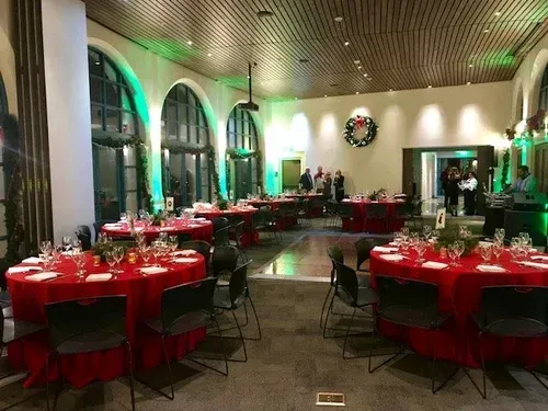 Elegant banquet hall with red tablecloths, round tables, and green-lit arched windows, set for an event
