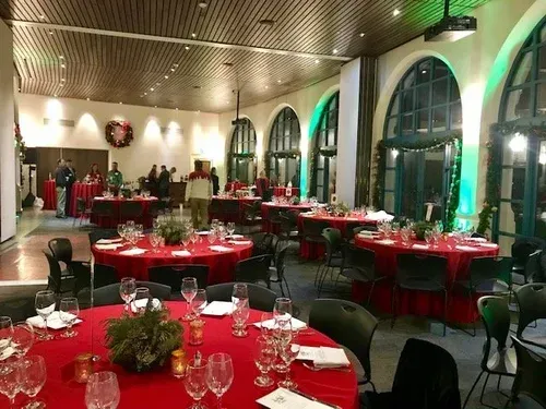 Elegant banquet hall with red table settings, white chairs, arched windows, and green accent lighting