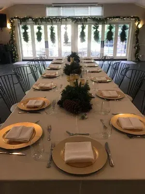 Elegant banquet table set for an event, with gold chargers, folded napkins, and greenery centerpieces in a bright room