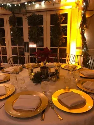 Round dining table set for a warm, candlelit dinner with gold chargers and folded napkins
