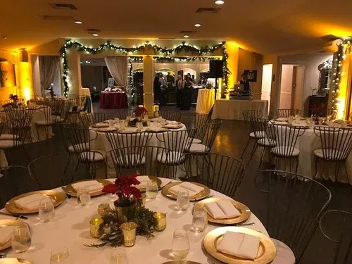 Elegant banquet hall with round, set tables and warm string lights around a decorated stage.