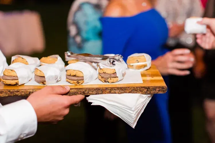 Tray of bite-sized desserts being served at a social event, with guests blurred in the background.