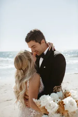 Couple embracing on a sunny beach, with white flowers in the foreground.