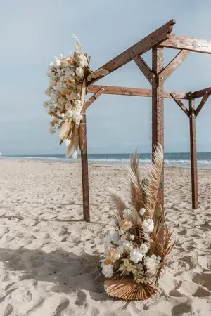 Beach wedding arch with white flowers and pampas grass on sand by the ocean