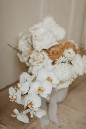 White and peach floral arrangement in a small white vase on a beige surface