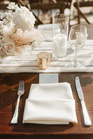 Elegant wedding table setting with white napkins, silverware, candles, and floral centerpiece