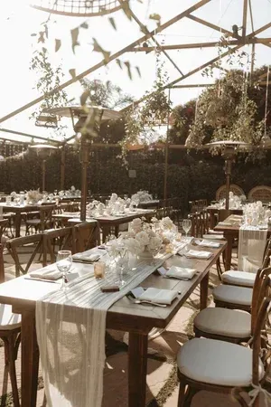 Elegant outdoor dining setup under a canopy with long tables, white chairs, and floral centerpieces