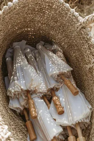 Several white bridal parasols with gold handles stacked in a woven basket