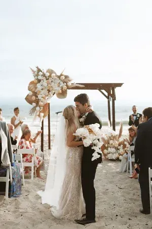 Beach wedding couple kissing under floral arch by the sea