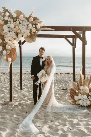 Wedding couple standing under a floral arch on a beach by the ocean