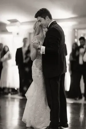 Couple slow dancing at a wedding reception, embracing on a reflective floor with guests blurred in the background
