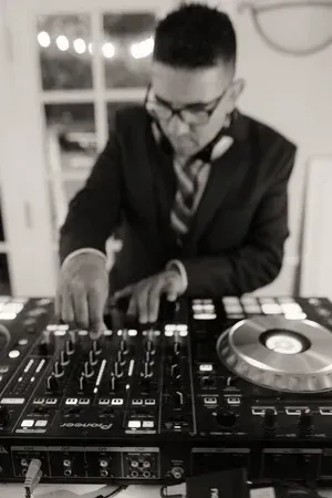 DJ in a dark suit adjusts controls on a mixer with a turntable in a black-and-white scene