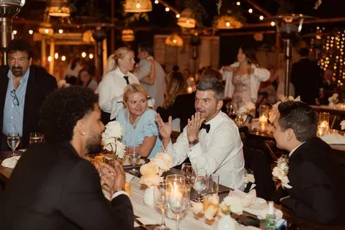 Guests chat at a candlelit dinner table under string lights.