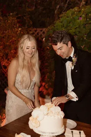 Bride and groom cut a white wedding cake at an outdoor evening reception.