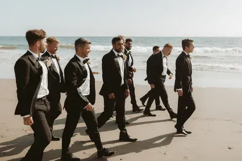Group of people in dark suits walking along a sunny beach by the ocean