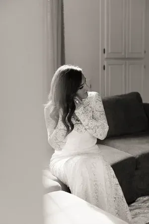 Woman in a white dress sitting on a sofa, turned sideways in a softly lit living room.