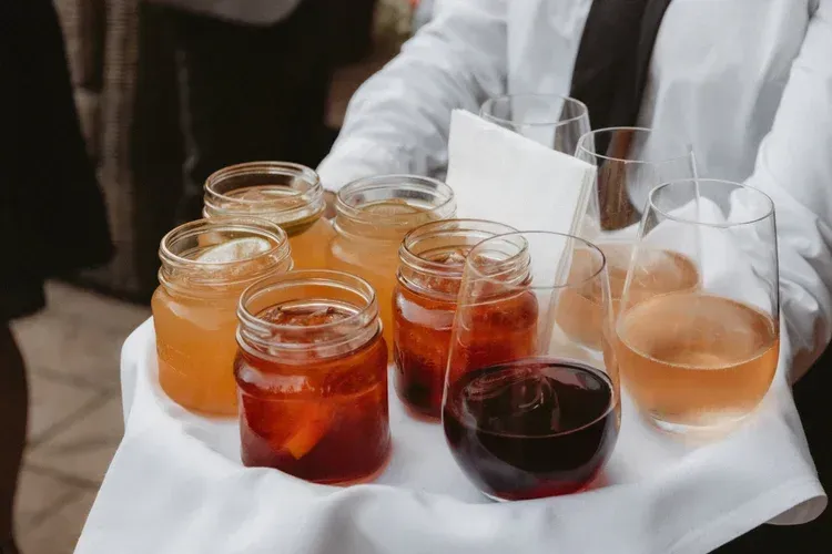Assorted drinks in jars and glasses on a tray held by a person in white