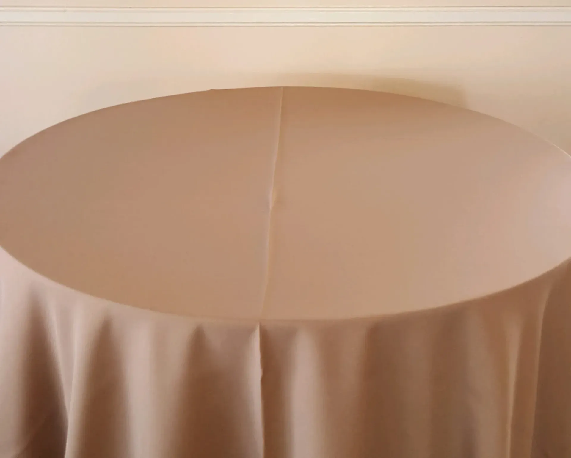 Round table covered with a beige tablecloth against a plain wall.