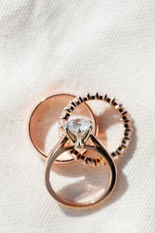 Three rings on white fabric: a rose-gold band, a diamond engagement ring, and a rose-gold ring.