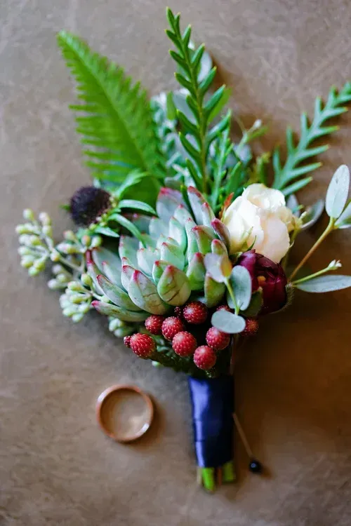 Small bouquet with green ferns, white and red flowers, and berries on a gray surface, tied with dark ribbon