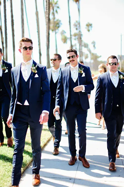Five men in navy suits walking outdoors on a sunny palm-lined street.