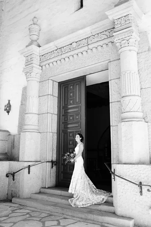 Bride in a white gown standing at a grand stone doorway holding a bouquet