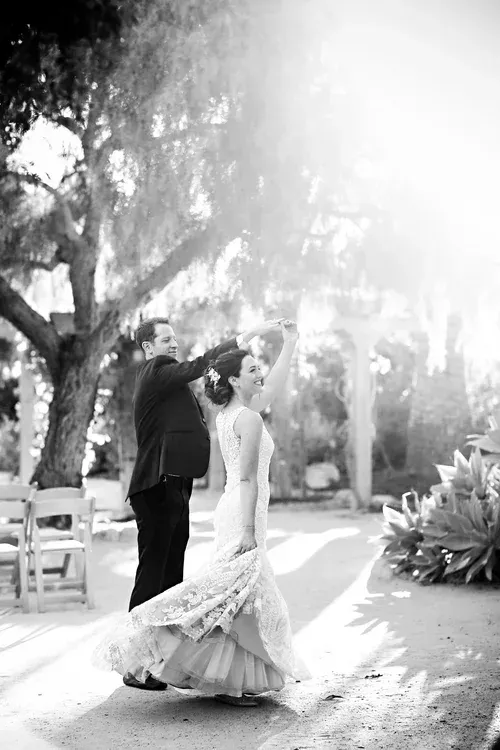 Bride and groom kissing outdoors in a sunlit garden, with the bride’s dress flowing behind her