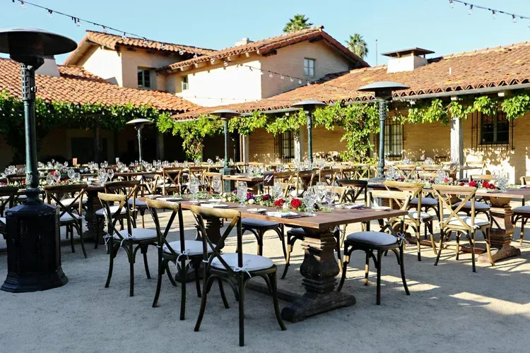 Outdoor restaurant courtyard with tables, chairs, and red-tiled buildings in the background