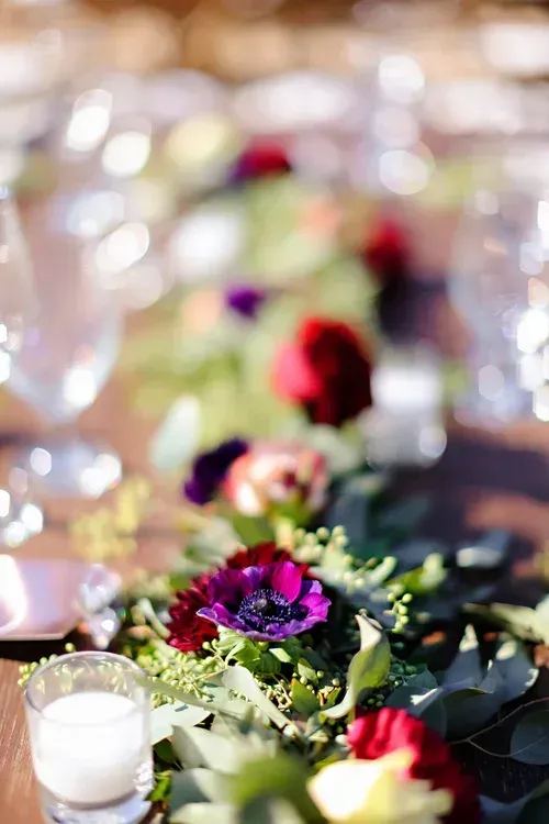 Floral table centerpiece with red, purple, and white flowers beside glassware at a formal event