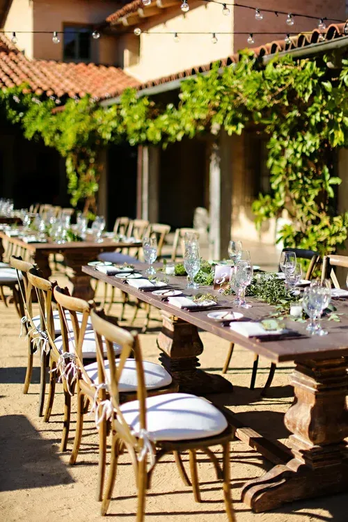 Outdoor dining tables under vine-covered pergola in a sunlit courtyard