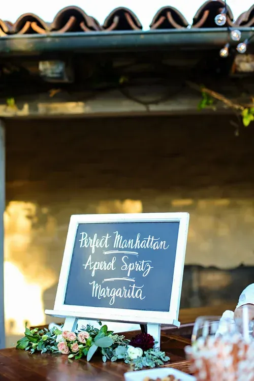 Black chalkboard sign on a floral-decorated table at a rustic outdoor wedding reception