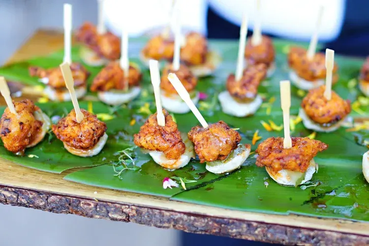 Skewered grilled appetizers on a banana leaf tray, topped with white sauce and toothpicks